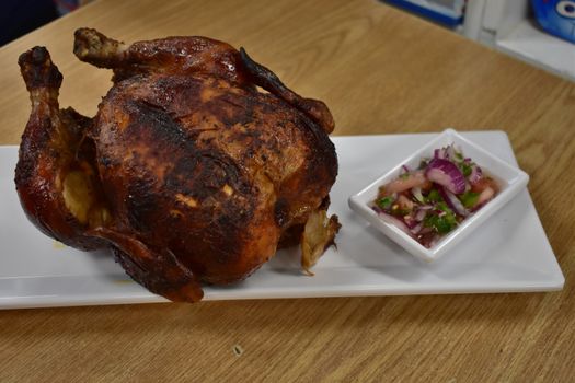 Rotisserie Chicken on a White Plate on a Wooden Table With Potatoes and a Small Salad Next to It