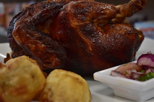 Rotisserie Chicken on a White Plate on a Wooden Table With Potatoes and a Small Salad Next to It