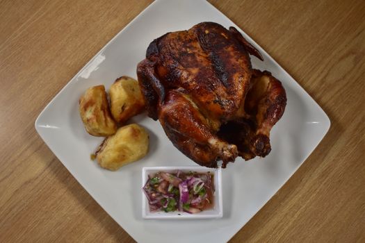 Rotisserie Chicken on a White Plate on a Wooden Table With Potatoes and a Small Salad Next to It