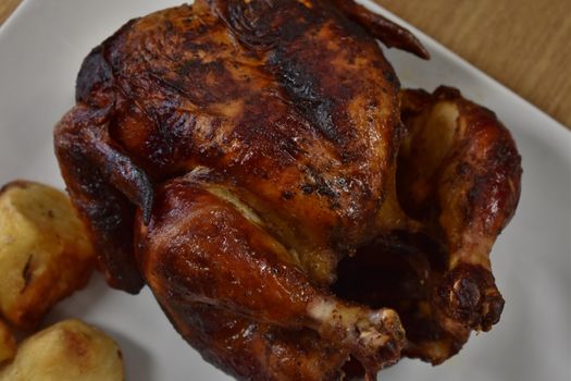 Rotisserie Chicken on a White Plate on a Wooden Table With Potatoes and a Small Salad Next to It