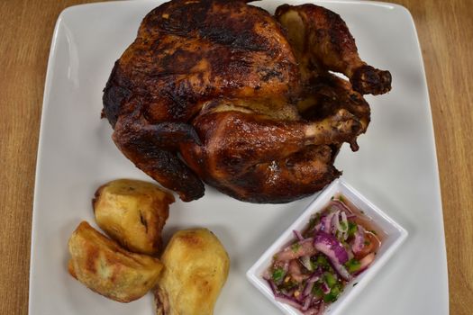 Rotisserie Chicken on a White Plate on a Wooden Table With Potatoes and a Small Salad Next to It