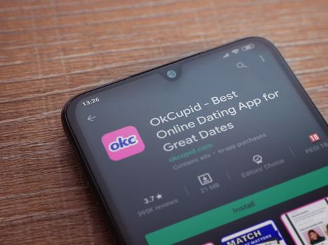 Lod, Israel - July 8, 2020: OkCupid app play store page on the display of a black mobile smartphone on wooden background. Top view flat lay with copy space.