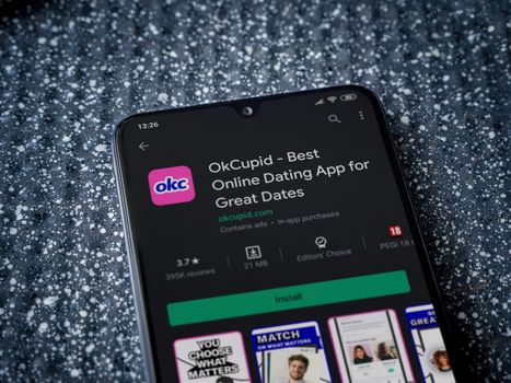 Lod, Israel - July 8, 2020: OkCupid app play store page on the display of a black mobile smartphone on a metallic background. Close up top view flat lay.