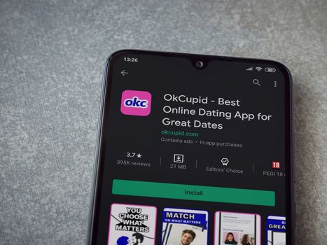 Lod, Israel - July 8, 2020: OkCupid app play store page on the display of a black mobile smartphone on ceramic stone background. Top view flat lay with copy space.