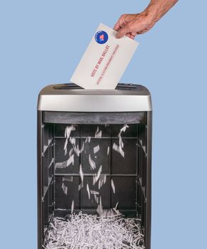 Vote by mail or absentee ballot being shredded in office paper shredder as illustration of voting fraud or lost votes in Presidential election