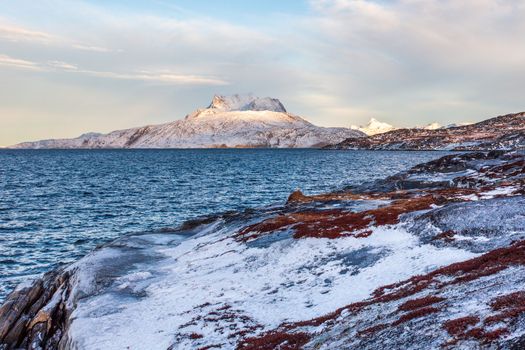 Frozen tundra landscape with cold greenlandic sea and snow Sermitsiaq mountain in the background, nearby Nuuk city, Greenland