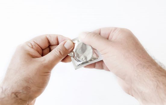 male hands while opening the package of a condom. Prevention of sexually transmitted diseases. Safe sex