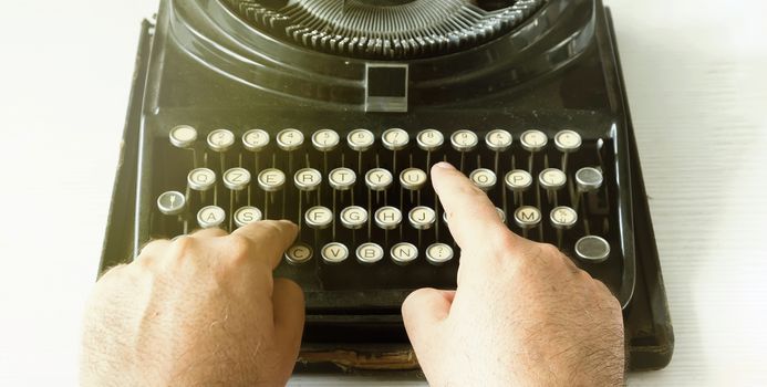 Male hands writing a text by typing the keys of an old typewriter. Vintage items and old mechanical technology