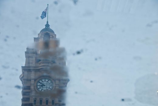 MELBOURNE, AUSTRALIA - JULY 29, 2018: Vintage classical Clocktower of Melbourne Flinders Street train station reflection from rain pond in a rainy day during mid Winter.