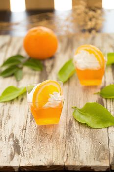 Orange jelly in a cup with whipped cream and orange sliced on black wooden background.