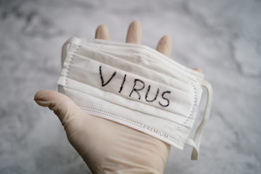 Hand holding medical protective mask with virus text.