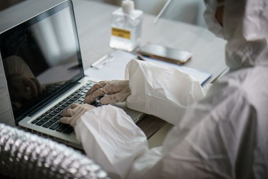 Woman in protective hazmat suit worker in laboratory computer analyzing in laboratory. to stop spreading coronavirus or COVID-19.