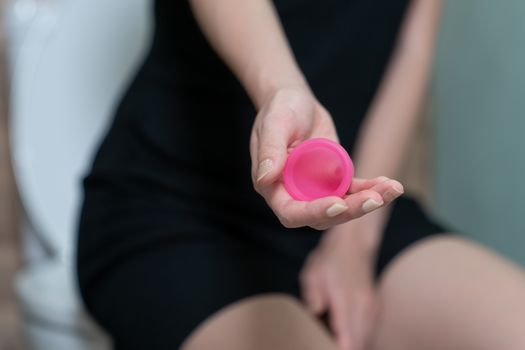 Woman hand holding menstrual cup in toilet. Selective focus. Concept of hygiene.