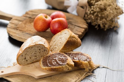 French bread baguette cut on wooden board with knife. with a chocolate butter and red apple.