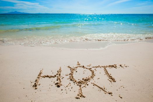 HOT word and sun symbol written on the sand of tropical sea beach