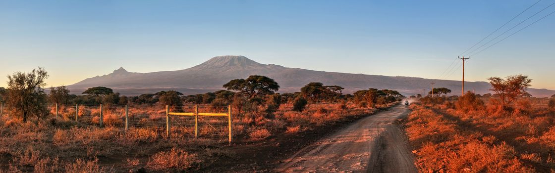 African landscape in red morning light, car coming on the road in distance with mount Kilimanjaro in background. Path near Kibo camp, Amboseli national park, Kenya