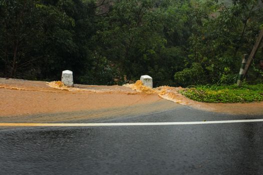 Water colored with yellow mud going down the road in large streams during heavy rain. Kandy, Sri Lanka