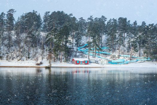 Empty waterslide with red beach hut near frozen lake on a cold winter day with snow in clouds. Sweden