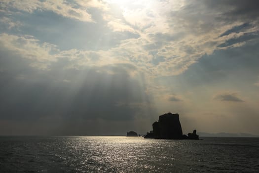 Sun rays shining on small deserted island in Andaman sea near Phi Phi, showing only silhouette of rock. Ao Nang, Thailand