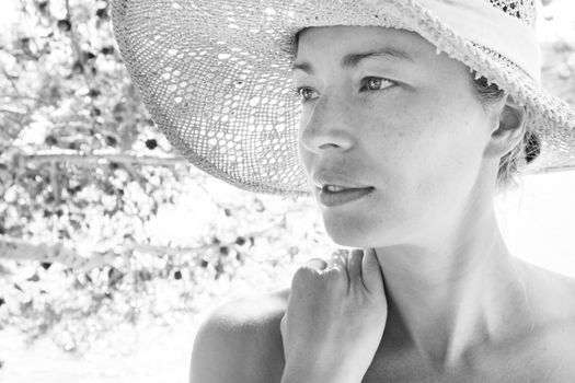 Close up portrait of no makeup natural beautiful sensual woman wearing straw sun hat on the beach in shade of a pine tree. Black and white image.