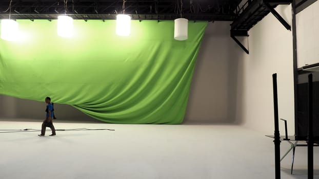 Big studio with green screen and lightman and soft box light hanging and white floor.