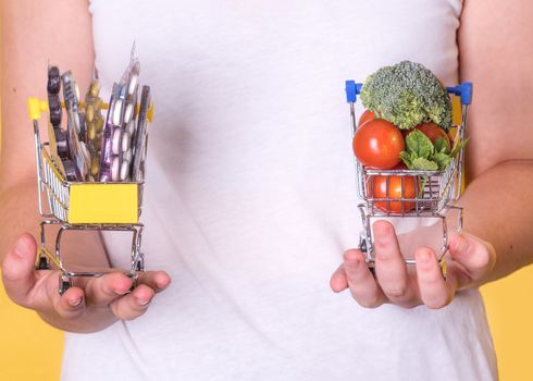 Hands holding shopping carts with vegetables and tablets on a yellow background, the concept of choosing healthy food and disease