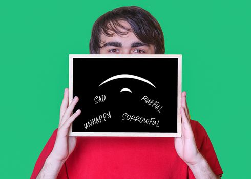 A young man holding chalkboard with the sign Sad on green background