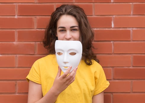 Young woman in yellow shirt putting on a mask against brick wall