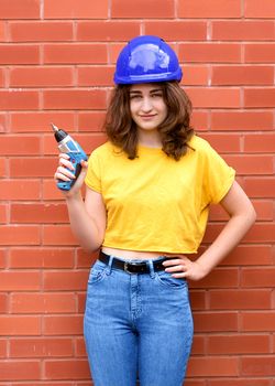 a female construction worker in yellow shirt and blue helmet with a screwdriver against brick wall