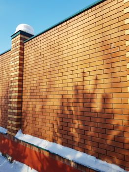 Modern red brick fence with turrets, in winter, outdoors.