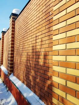 Modern red brick fence with turrets, in winter, outdoors.