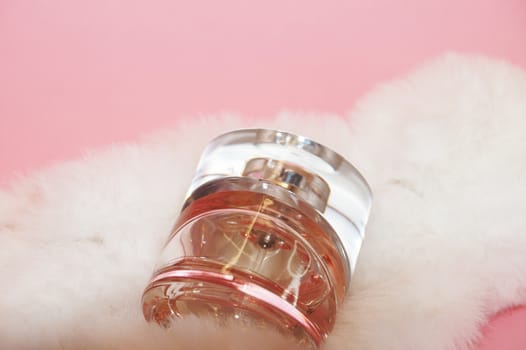 perfume bottle and white fur on a pink background close-up