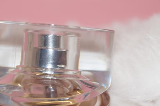 perfume bottle and white fur on a pink background close-up