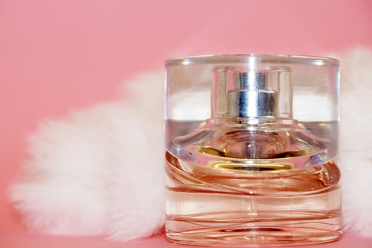 perfume bottle and white fur on a pink background close-up