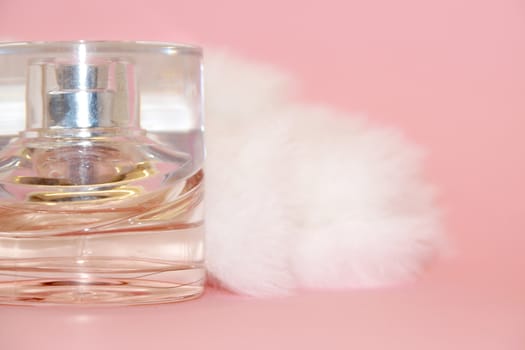 perfume bottle and white fur on a pink background close-up
