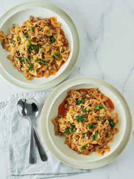 Pasta Farfalle with tomato sauce and ground meat in plate on white marble tabletop. Idea and recipes for easy, simple dinner one-pot meat goulash. Top down view or flat lay. Vertical. Copy space