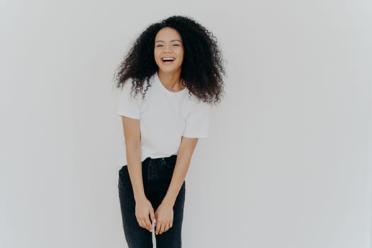 Studio shot of joyful African American woman laughs happily, dressed in casual wear, feels good, poses against white background with blank space for your advertising content, feels energized