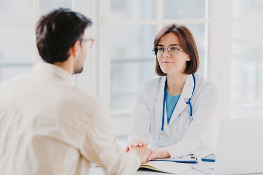 Male patient has consultation with female doctor, receives support, finds out about serious disease. Woman therapist comforts ill visitor in office or consulting room, talk about how to cure illness