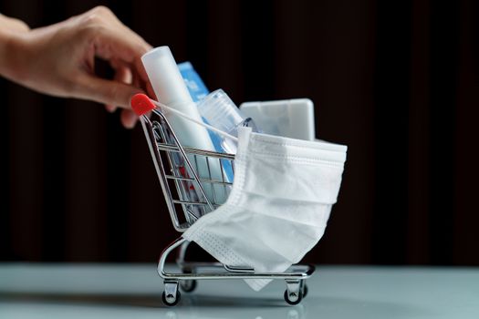 Hands pushing shopping cart and sanitizer products with protective face mask corona virus or Covid-19 protection.