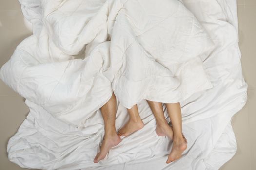 Close up of male and female feet on a bed having sex under sheets in the bedroom.