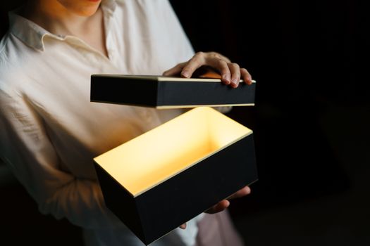 Woman opening a box with gold light mean something exciting inside.
