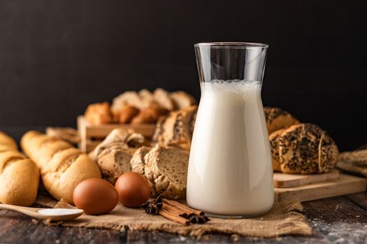 Milk in a glass bottle placed on a wooden table with ingredients for making bread and bakery