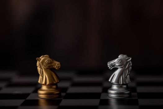 silver and gold horse of the chess in the game on board with wooden background.