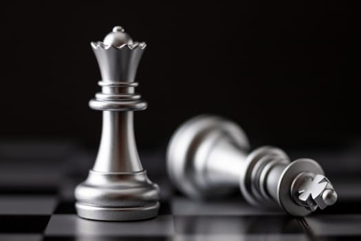 Silver queen standing and king falling in game on the chessboard