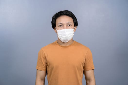 Portrait of asian man wearing face surgical mask on blue color background; Coronavirus pandemic; covid19 outbreak; social distancing and responsibility; healthcare and protection against virus concept