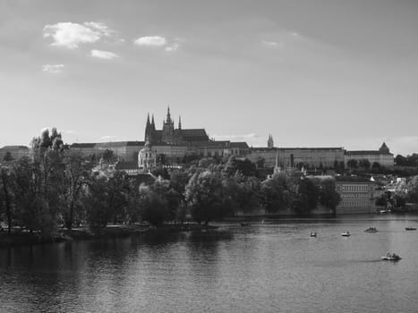 panorama of Charles bridge over Vltava river and Gradchany, Prague Castle and St. Vitus Cathedral. Czech Republic, summer sunny day, tourists relaxing on pedal boats, black and white.