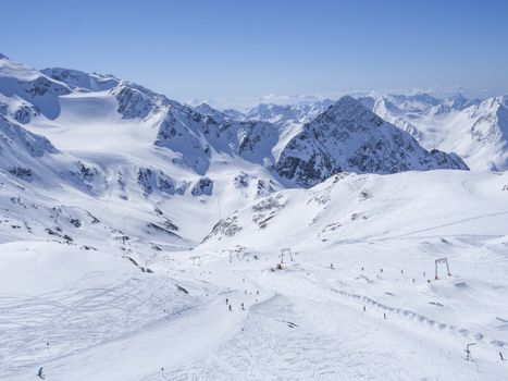 Winter landscape with snow covered mountain slopes and pistes with skiers enjoying spring sunny day at ski resort Stubai Gletscher, Stubaital, Tyrol, Austrian Alps.