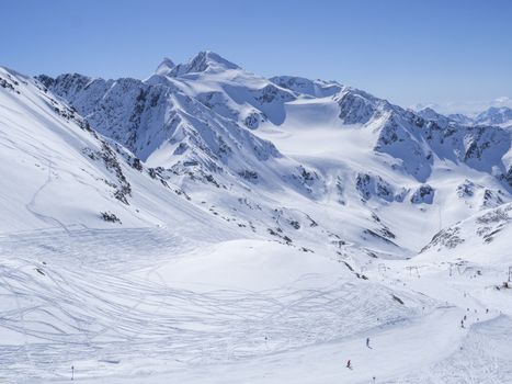 Winter landscape with snow covered mountain slopes and pistes with skiers enjoying spring sunny day at ski resort Stubai Gletscher, Stubaital, Tyrol, Austrian Alps.