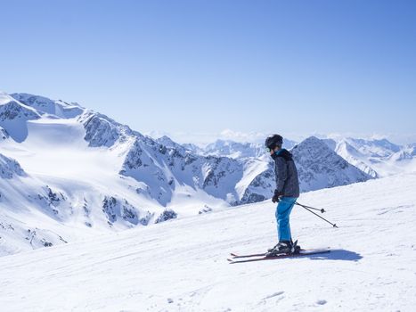 Skier at the top of Schaufelspitze mountain at Stubai Gletscher ski resort preparing to go down into the valley. Snow covered peaks. South Tyrol, Austrian Alps. Nature and sport background, blue sky sunny spring day.