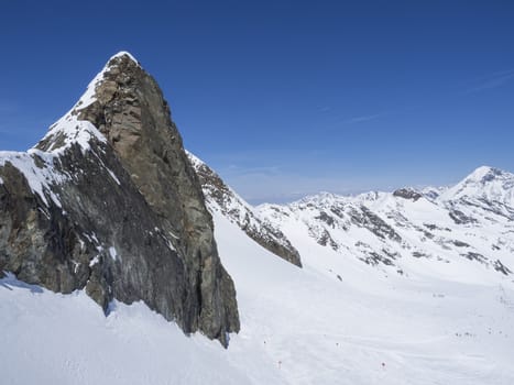 Winter landscape with sharp mountain peak and snow covered slopes and pistes with skiers enjoying spring sunny day at ski resort Stubai Gletscher, Stubaital, Tyrol, Austrian Alps